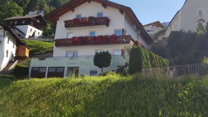 En traditionel bygning i alpehusstil med en hvid facade, træbalkoner og et skilt med teksten "Gästehaus WALCH".