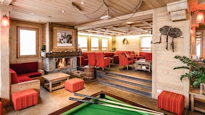 Eine gemütliche Lounge mit Holzboden, einem Billardtisch, roten Polstersesseln und einem Kamin.
