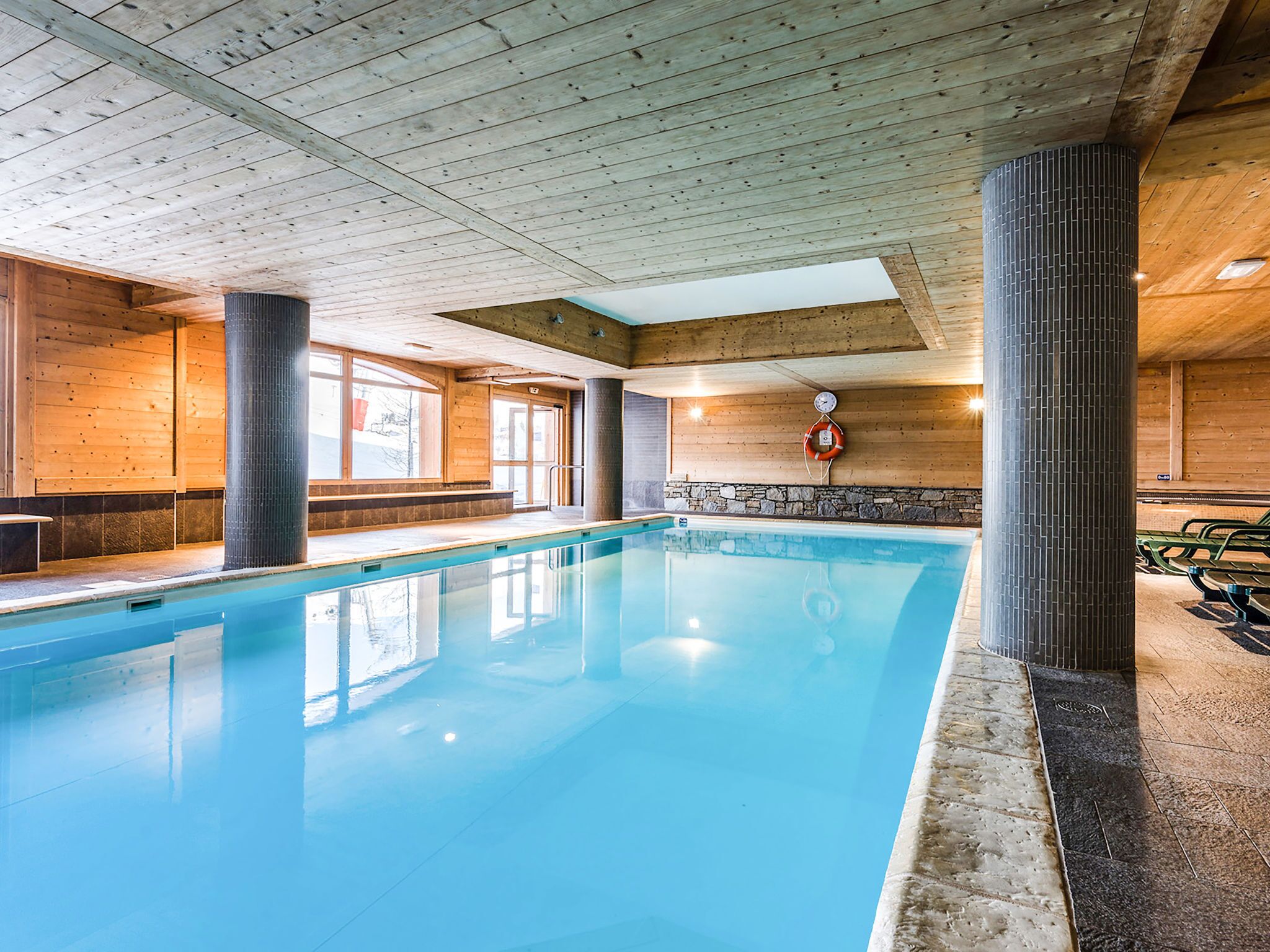 An indoor swimming pool with wooden walls and ceiling, stone accents, and a lifebuoy on the wall.