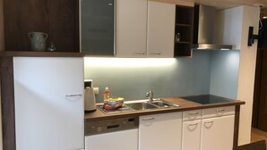 Cocina compacta con muebles blancos, un lavamanos de acero inoxidable y lavavajillas.