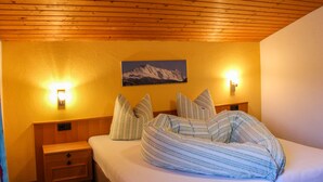 Un dormitorio con techo de madera, una cama con ropa de cama a rayas, dos mesitas de noche y un cuadro de un paisaje montañoso en la pared.