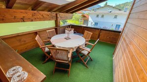 Una terraza de madera con una mesa redonda y sillas, rodeada de césped artificial verde.