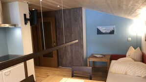 Una habitación compacta con una mesa de madera para comer, una cama con ropa de cama a rayas, una mesita con una silla y un televisor instalado en la pared.