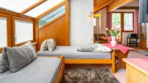 A cozy room with a wooden ceiling, two single beds, a dining table with chairs, a small kitchen area, and a window with blinds. - Rosi Studio by Interhome (Sölden)