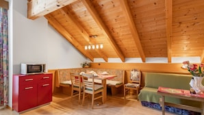 Un espai loft acollidor amb sostre de fusta, zona de menjador amb taula i cadires, un armari vermell i un sofà verd.