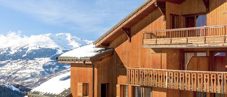 Een houten chalet met balkons, een met sneeuw bedekte berg op de achtergrond en een heldere lucht.
