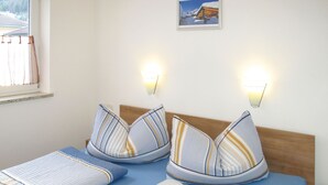 A hotel room with two beds, striped bedding, a wooden headboard, a nightstand, a lamp, and a framed picture on the wall. - Amethyst by Interhome (Sölden)
