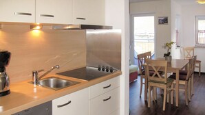 A compact kitchen with a built-in stove, sink, and dishwasher, leading to a dining area with wooden chairs and a table. - Amethyst by Interhome (Sölden)