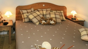 Un dormitorio con cama, almohadas, un osito de peluche, una lámpara, una mesita de noche y un ovillo de lana.