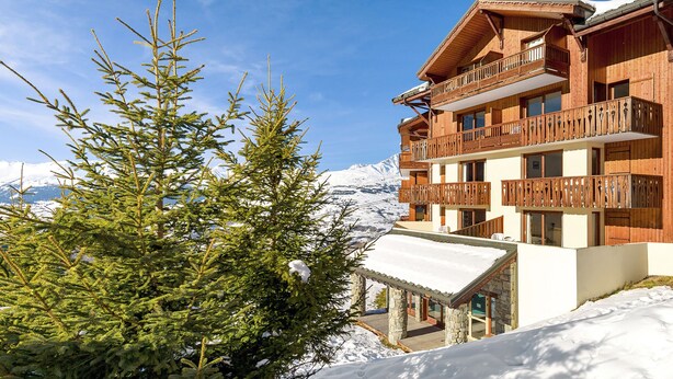 Una cabaña de madera con balcones, rodeada de nieve y árboles de hoja perenne.