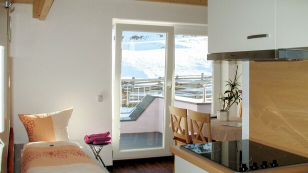 Una habitación pequeña y acogedora con cama, kitchenette y vista a un paisaje nevado a través de una puerta corrediza de vidrio.