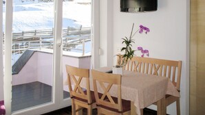 Una habitación con una mesa y sillas de madera, un televisor montado en la pared y vistas a un paisaje nevado a través de un ventanal.