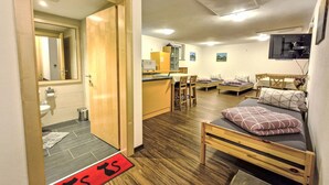 Kompakti hotellihuone, jossa on pieni keittiö, ruokailutila ja sänky, jonka edessä on punainen eteismatto.