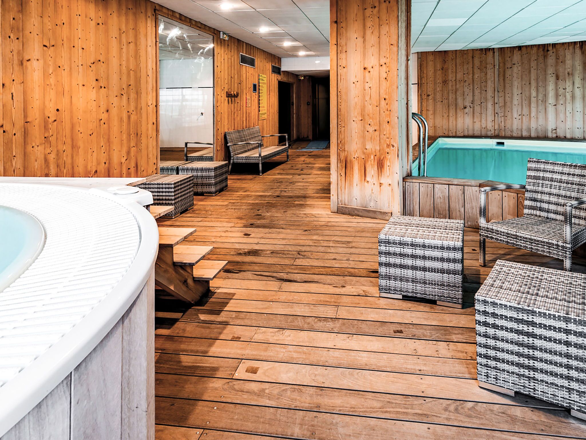 A spa area with wooden flooring, a hot tub, and wicker furniture.