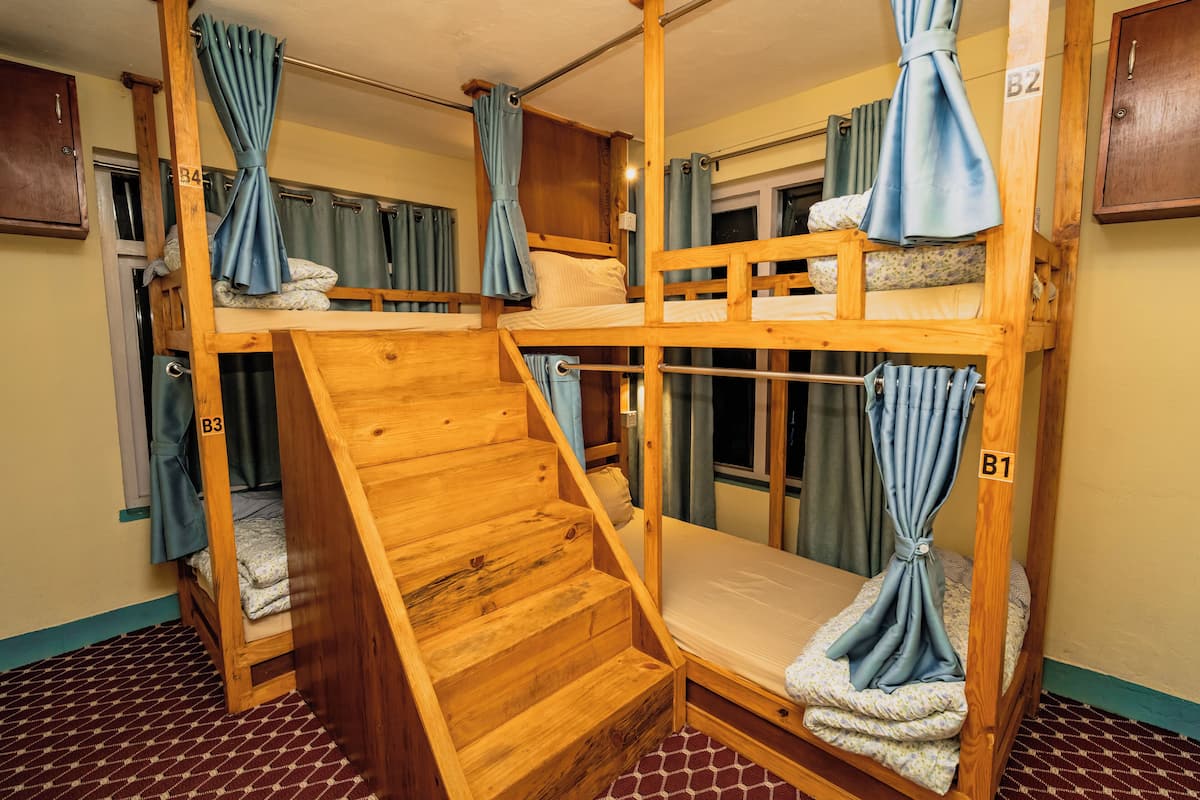 A bunk bed room with wooden construction, a small staircase, and curtains on the windows.