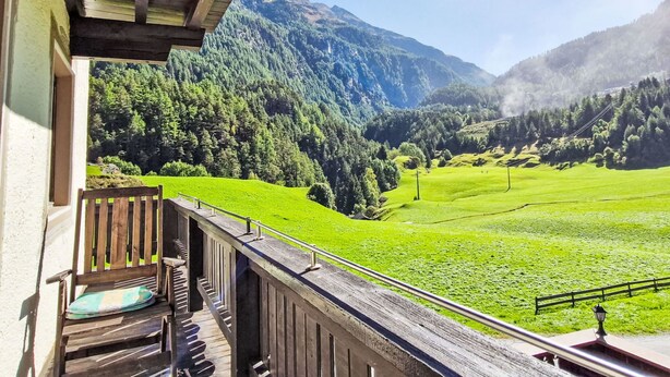 En balkon med trægelænder der kigger ud over en grøn dal og bjerge.