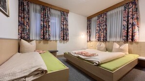 A hotel room with two single beds, floral curtains, a small bedside table, and a wall-mounted light. - Wildmoos by Interhome (Sölden)