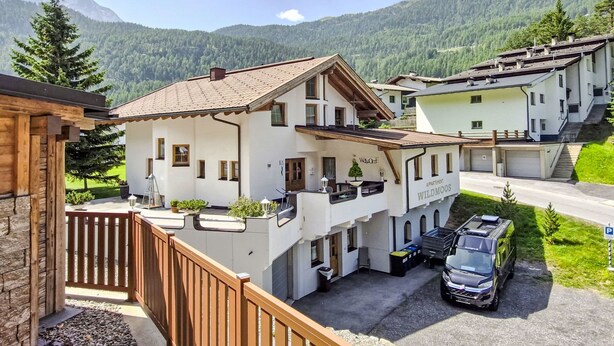 A white building with a balcony, labeled "Welcome Wildmoos," and a parked vehicle in front. - Wildmoos by Interhome (Sölden)