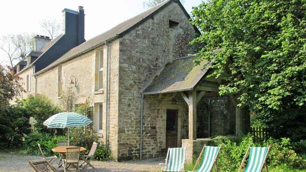Un bâtiment en pierre doté d’un jardin comprenant une table, des chaises et un parasol.