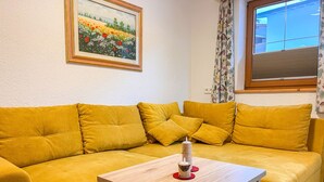 Un sofà groc amb una taula de centre de fusta en una habitació amb un quadre a la paret i una finestra amb cortines.