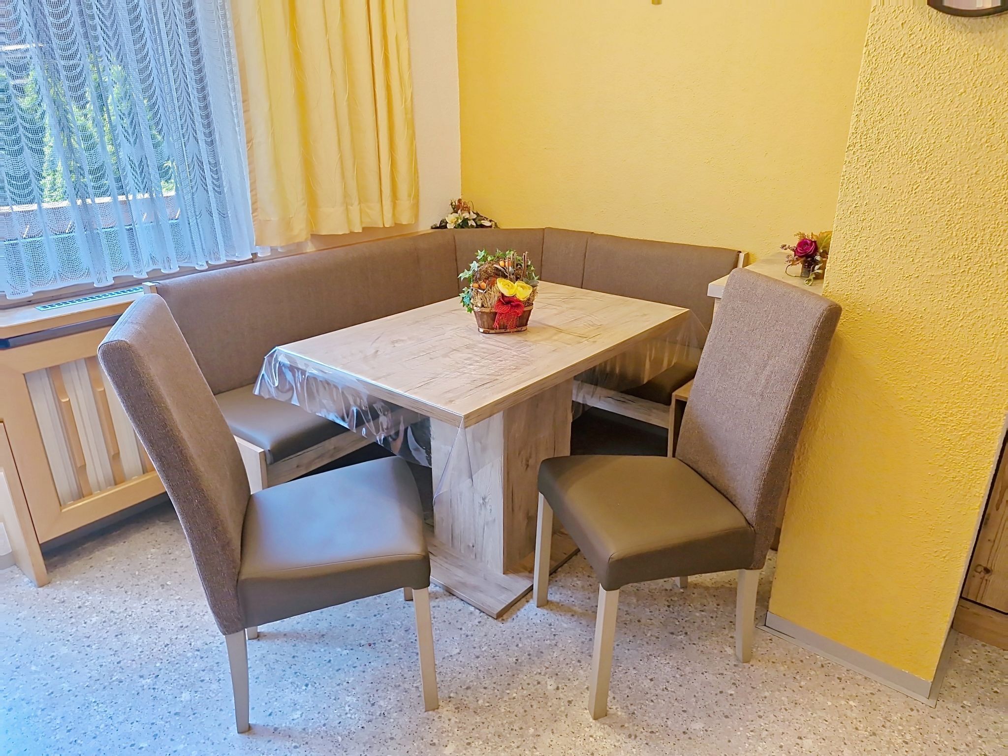 A corner dining area with a wooden table, cushioned chairs, and a small potted plant on the table.