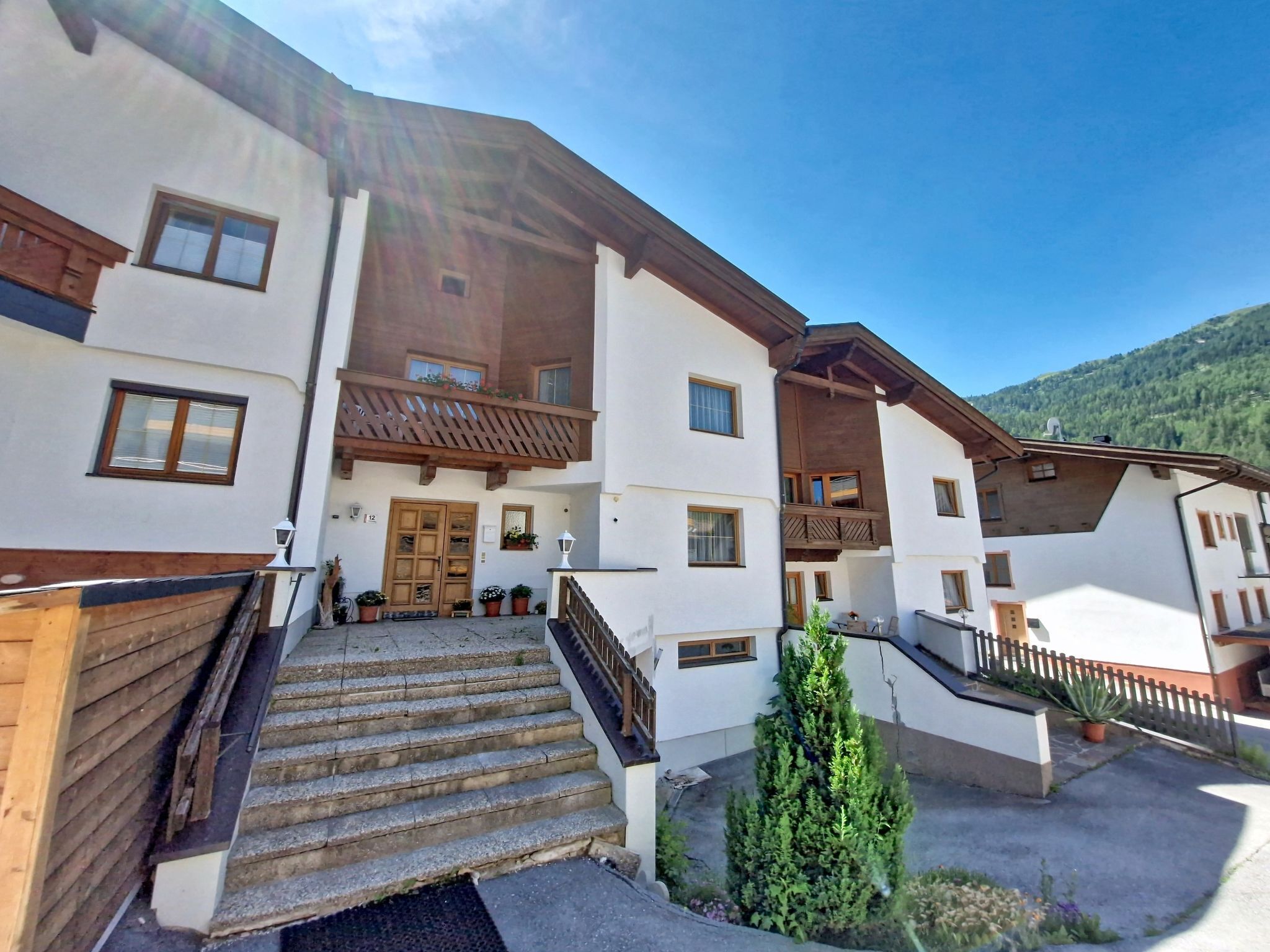 A multi-story building with a wooden staircase, balconies, and a mountain backdrop.