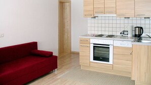 A compact kitchen with wooden cabinets, a built-in oven, and a red sofa.