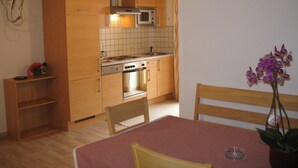 A compact kitchen with wooden cabinets, a microwave, and a stove. There is a dining table with chairs and a potted orchid. - Birkenheim by Interhome (Sölden)