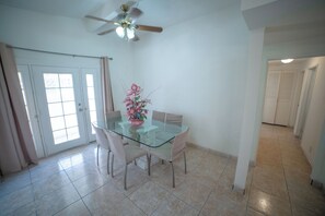 Enjoy meals in this dining area with a glass-top table and four chairs, surrounded by a ceiling fan and a vase with fresh flowers.