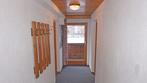 Un couloir étroit avec un plafond en bois et un sol recouvert de moquette, qui mène à une porte donnant sur un espace ext érieur enneigé.
