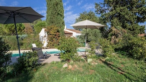 Un patio trasero con piscina, dos sombrillas y sillas de descanso.