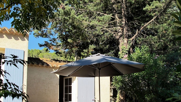 Un patio exterior con una mesa, sillas, una sombrilla y vistas a una casa con tejado de baldosas y una puerta azul.