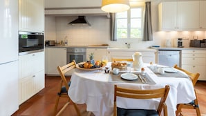 Una cocina moderna con armarios blancos, una isla central con productos para el desayuno y un comedor con una mesa preparada para dos.