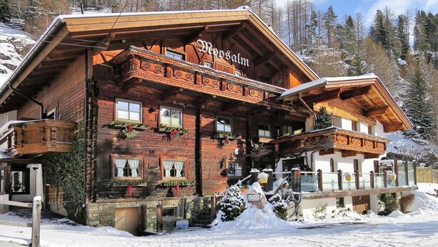A wooden chalet with a balcony, named 'Merdsalm', surrounded by snow-covered trees.