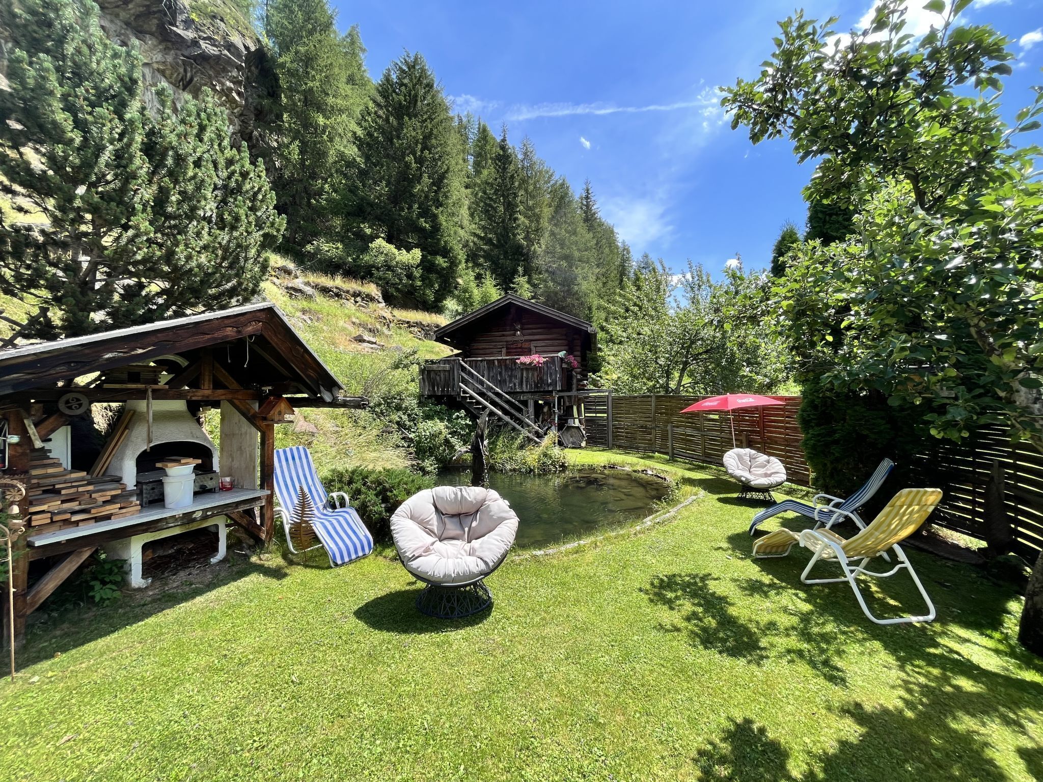 A rustic outdoor area with a wooden structure, a small pond, and lounge chairs.
