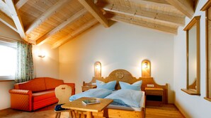 A cozy room with a wooden ceiling, a bed with a headboard, a small table, a chair, and a red sofa.