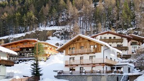 Un chalet de montagne doté de plusieurs balcons en bois, d’un mur en pierre et surplombant un paysage enneigé.