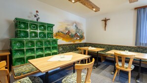 Un restaurant avec des tables et des chaises en bois, un mur décoré d’une mosaïque verte et une fresque représentant un cheval et une montagne.