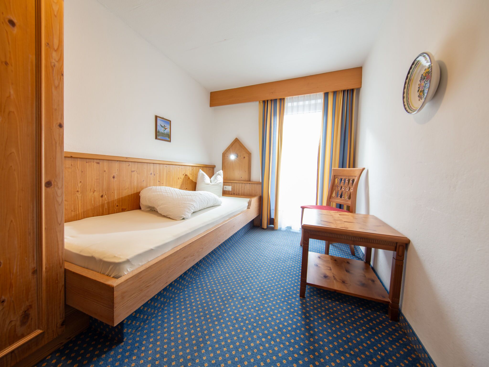 A small, cozy room with a single bed, a wooden nightstand, and a small table.