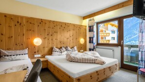 Een slaapkamer met houten lambrisering, twee bedden, een bureau en een raam met uitzicht op gebouwen en bergen.