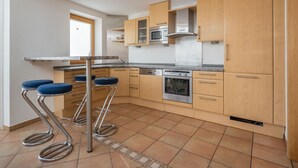 Una cocina moderna con armarios de madera, horno empotrado y campana extractora de acero inoxidable. Hay dos taburetes de bar con asientos azules.