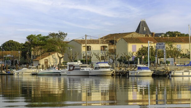 A marina with several boats docked, a building with a tiled roof, and a sign indicating 'Acta Nautica Ville de Fleury'.