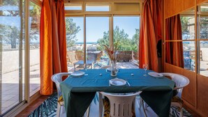 A dining area with a table set for two, large windows with curtains, and a view of the outdoors.