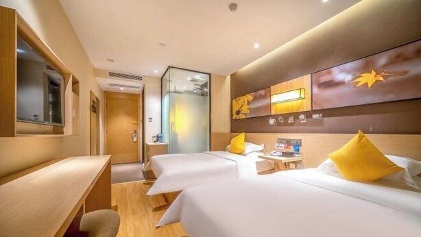 Ein Hotelzimmer mit zwei Betten, einem Schreibtisch, einem Spiegel und einer Wand mit Symbolen, die Annehmlichkeiten darstellen.
