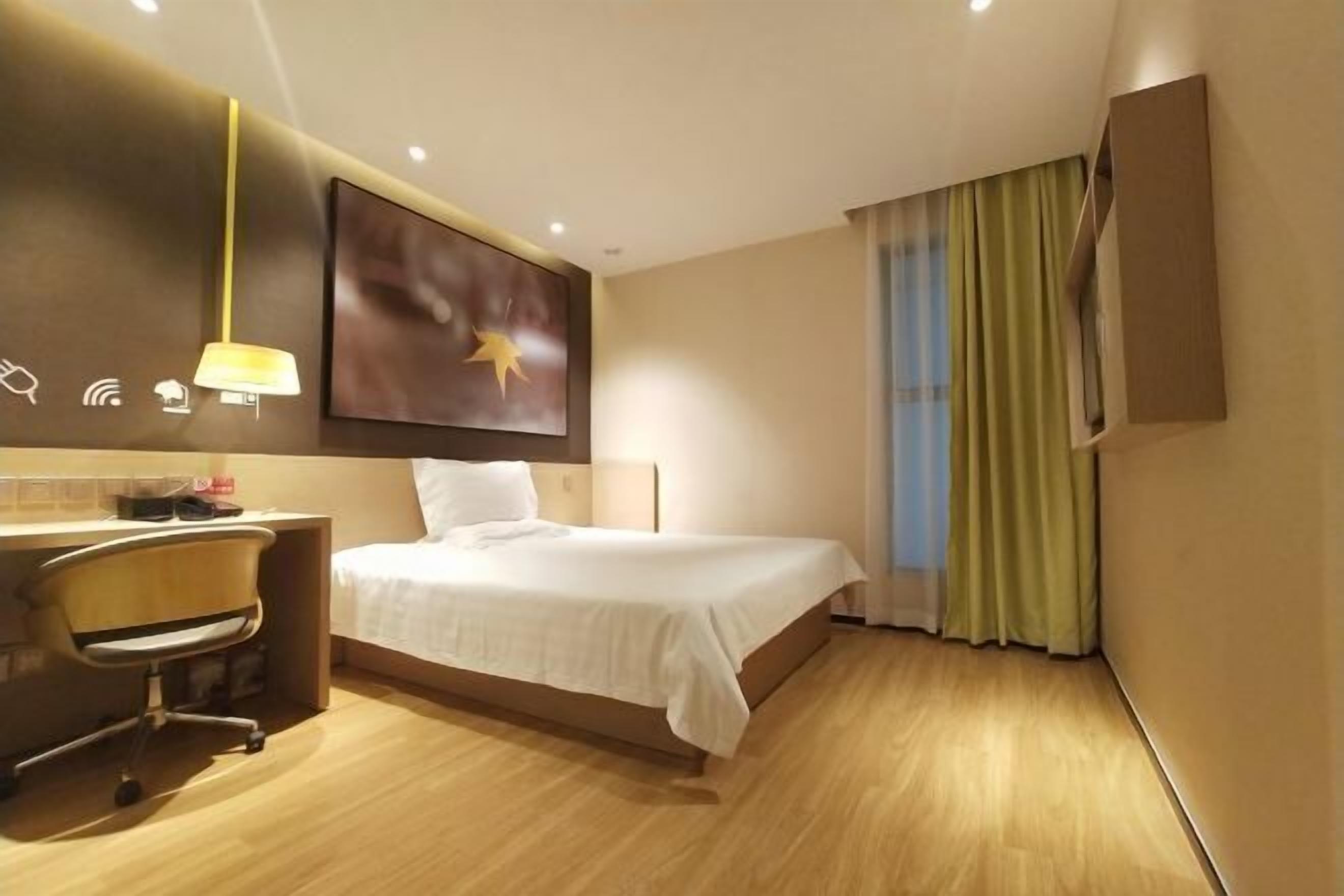 A hotel room with a bed, desk, chair, and a painting on the wall.