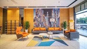 Eine moderne Lobby mit einer großformatigen Stadtansichtsmalerei, einer Sofagarnitur mit orangefarbenen Kissen, einem runden Couchtisch und einem Bücherregal.