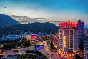 A hotel with multiple floors, a prominent entrance, and a view of surrounding buildings and hills. - XiYueli Hotel(Guiping Xishan store) (Guiping)