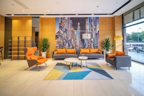 A hotel lobby with a cityscape mural, orange seating, a coffee table, and a large window. - XiYueli Hotel(Guiping Xishan store) (Guiping)