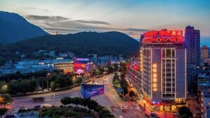 A hotel with a prominent red sign on the top, surrounded by other buildings and a mountain in the background. - XiYueli Hotel(Guiping Xishan store) (Guiping)