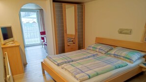 Quarto com cama, chão de madeira, escrivaninha com computador, espelho e porta de correr para uma varanda.